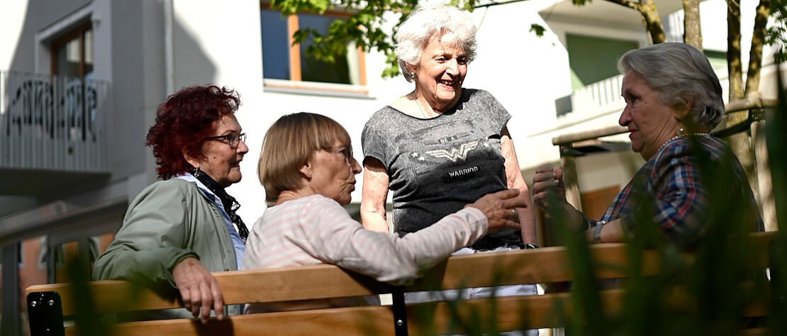 Vier Seniorinnen auf einer Bank im Garten, die miteinander reden
