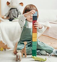 Kind das am Boden sitzt und einen Turm mit Holzklötzen baut