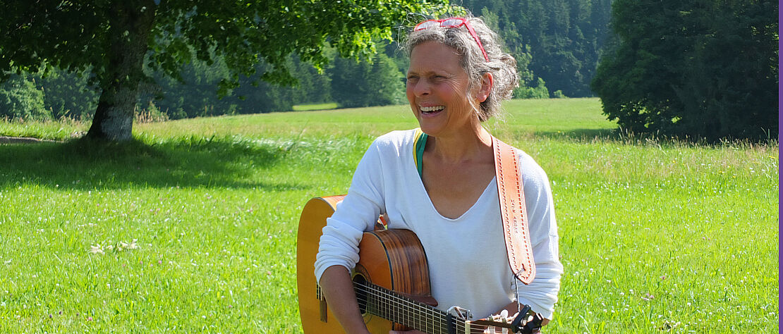 Gabriele Wanger steht auf einer gründen Wiese mit Gitarre 