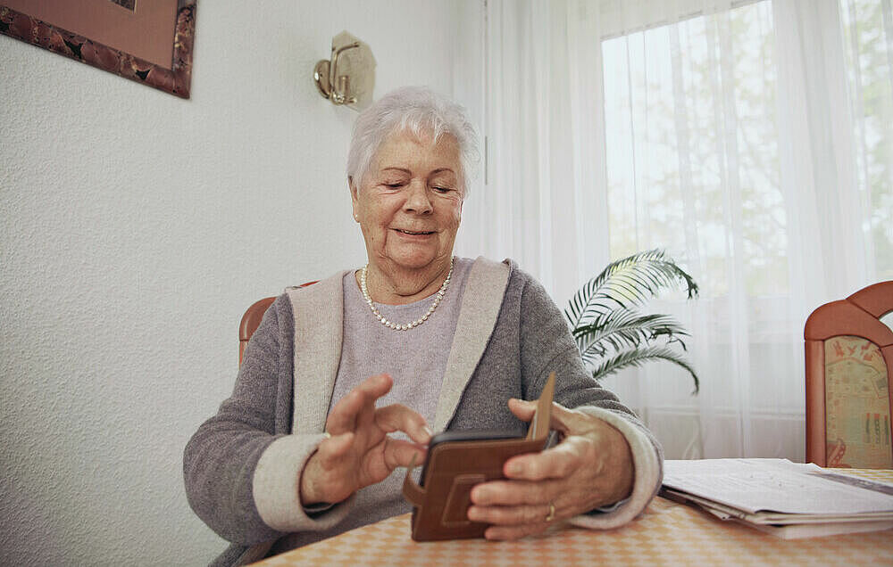 Seniorin die an einem Tisch sitz mit dem Handy in der Hand.