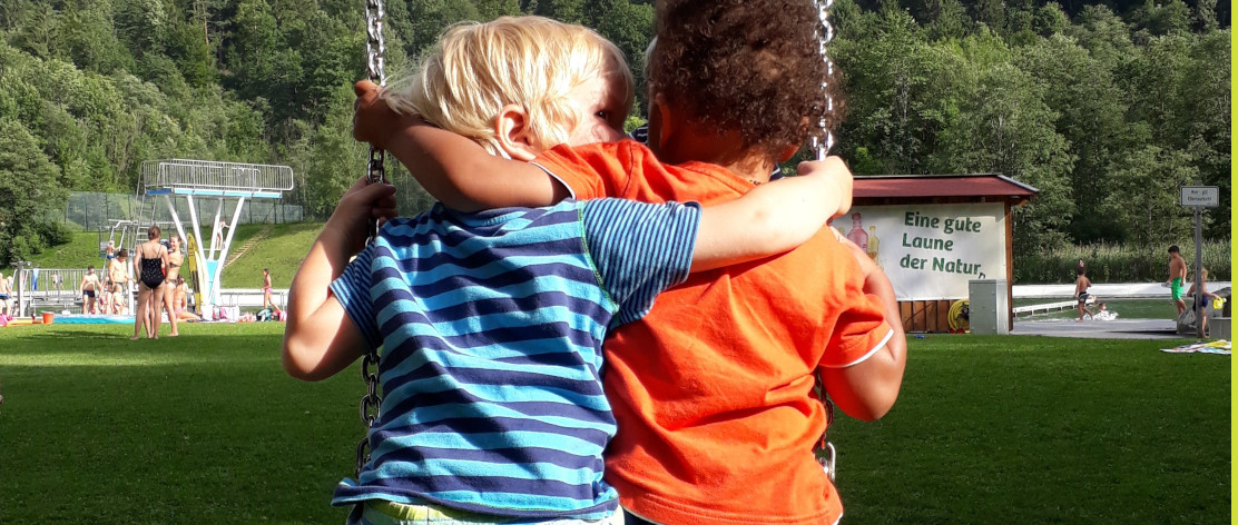 zwei Kinder, die sich umarmen und auf einer Schaukel sitzen