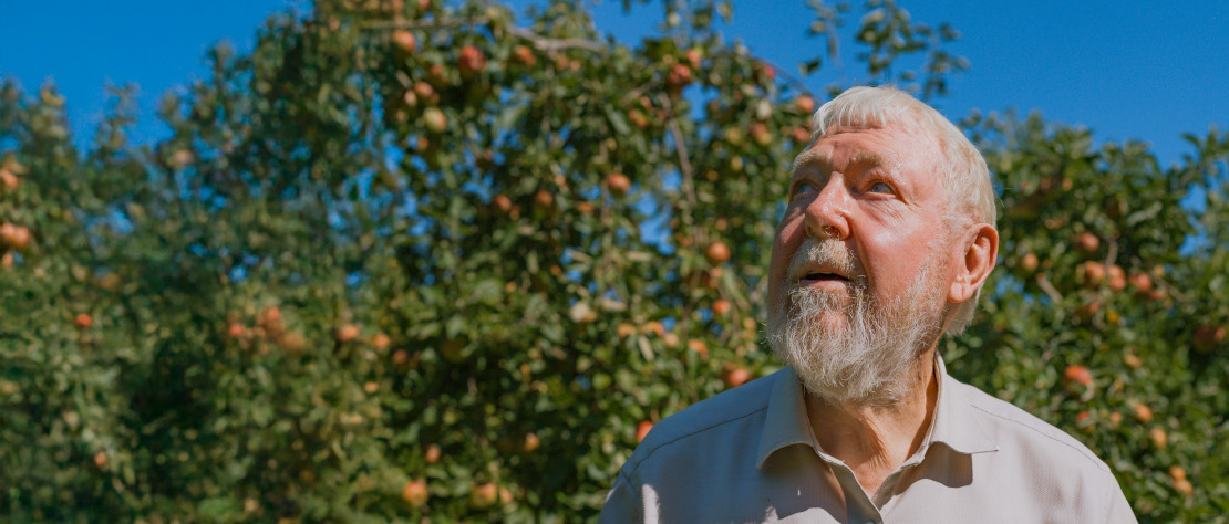 Michael Succhow steht vor einem Apfelbaum mit rote Äpfeln und einem blauen Himmel